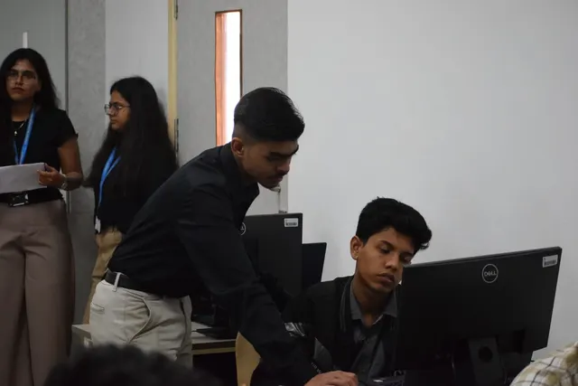 A person in black leaning in to help a participant at a computer