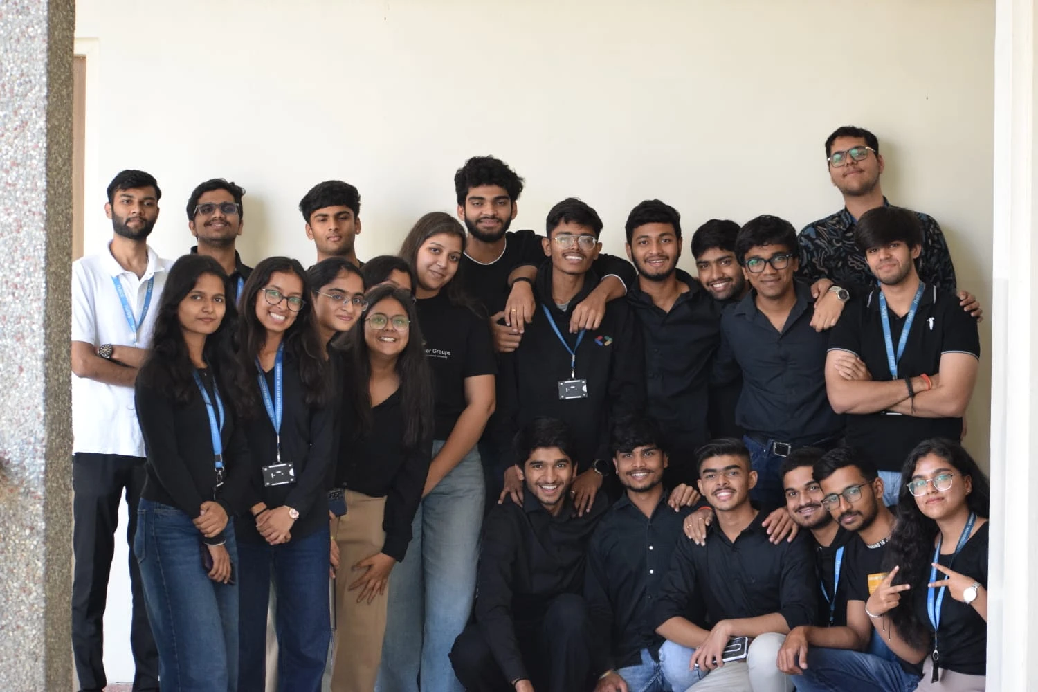 A large group of students in black, many wearing university lanyards, posing against a white wall
