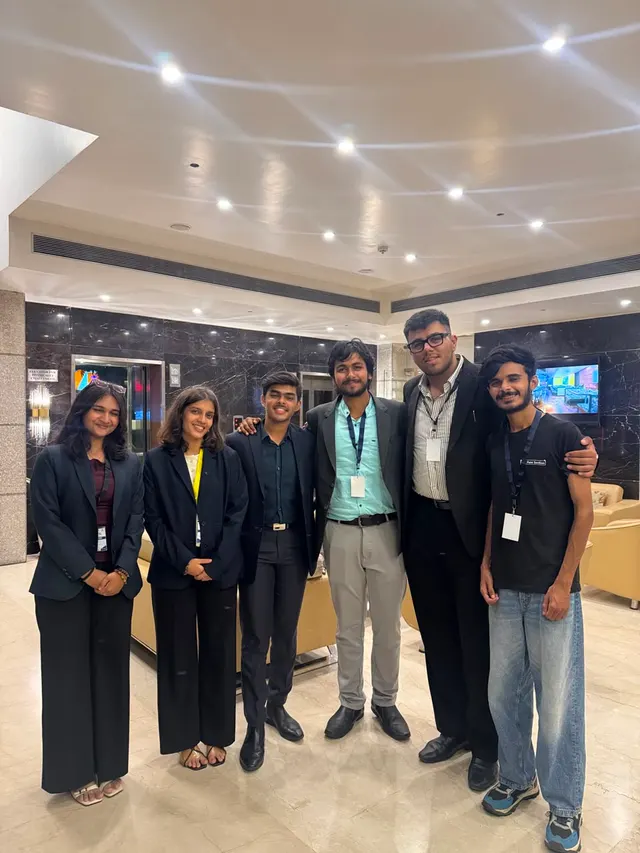 Six people in blazers and lanyards standing together in a hotel lobby