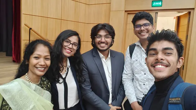 A group selfie of five people in an auditorium